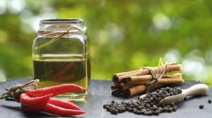 glass jar of oil, spicy red peppers, cinnamon sticks, and black peppercorns