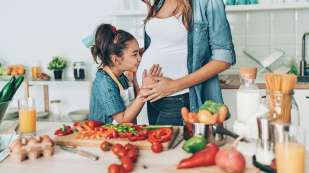 young girl kissing her pregnant mothers belly while preparing food in the kitchen