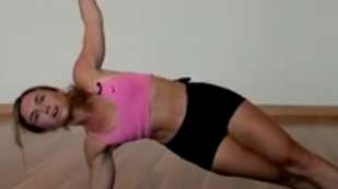 female presenting in a pink workout top and black workout shorts in a side raised yoga position on a yoga mat