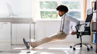 dark skinned male presenting person stretching using his desk chair  