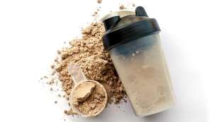 protein powder on table, in scoop with a shaker bottle next to it filled with protein powder drink