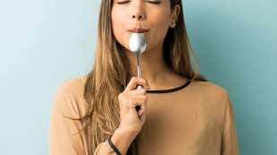 woman standing with eyes closed with tip of a large spoon in her mouth like she's eating a popsicle