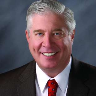 headshot image of Jim Emme, a white older male, smiling in a suit and red tie