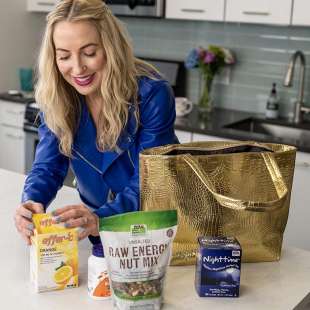 DJ Blatner in her kitchen with a gold purse opening Effer-C, Raw Energy Nut Mix, and Nighttime Tea.
