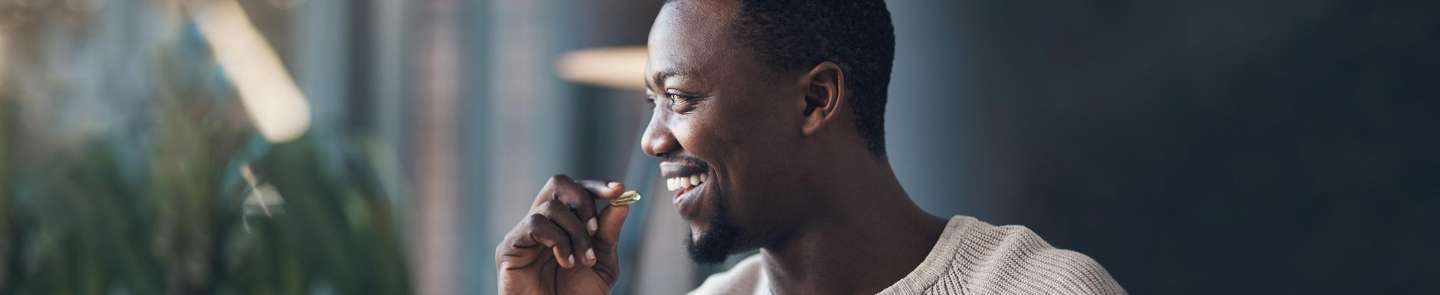 dark skinned male presenting person smiling and taking a vitamin