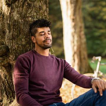 man leaning against tree, with his eyes closed. Red shirt, peaceful