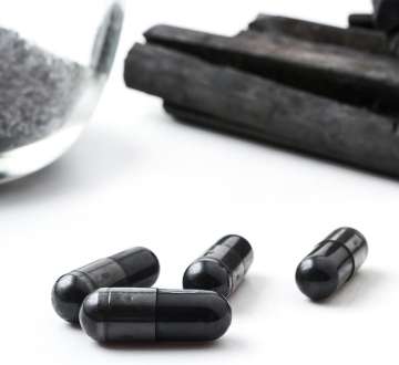 few pill capsules of activated charcoal with charcoal sticks in the background