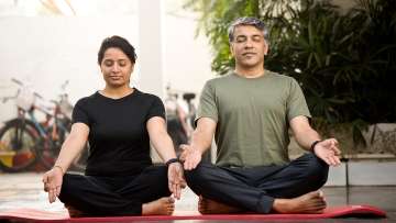 medium skinned female and male presenting persons sitting on the floor, legs crossed, hand on knees in meditation pose