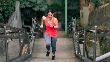 medium skinned female presenting person in a red tank top running up set of outdoor stairs