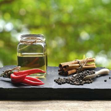 glass jar of oil, spicy red peppers, cinnamon sticks, and black peppercorns