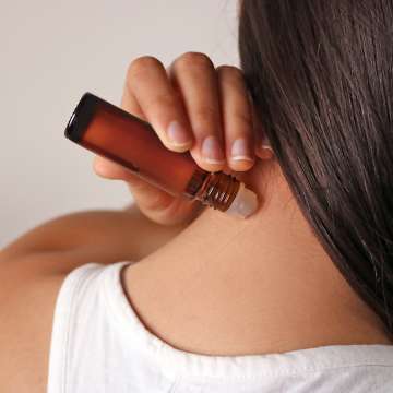 Light skinned female presenting person applying essential oils from a roller ball onto her neck. 