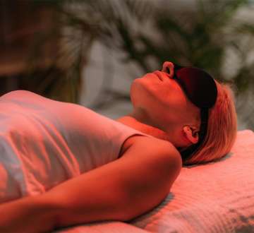female presenting person lying on a table with eye mask on bathed in red light