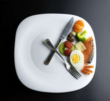 white plate with forks and knives laid out like clock hands with food inside the hands
