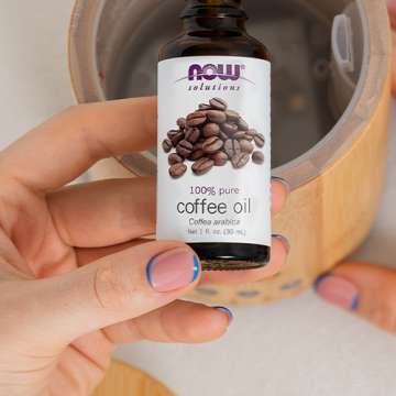 top view of bamboo essential oils diffuser with light skinned hands holding NOW Coffee Oil