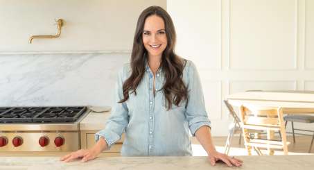 Kelly LeVeque Standing in her kitchen in a light blue shirt