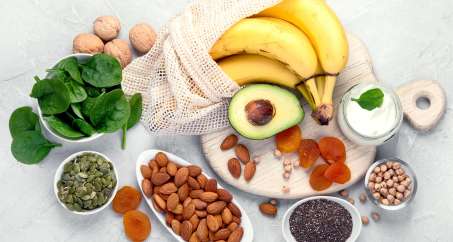 Assortment of fruits, nuts, seeds and vegetables including spinach, bananas, avocado, almonds, pumpkin seeds, etc. 