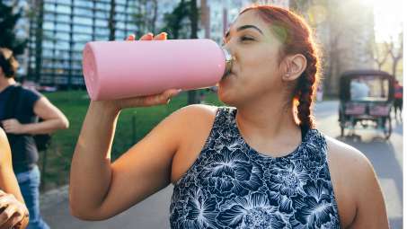 medium skinned female presenting person drinking water out of large pink water bottle