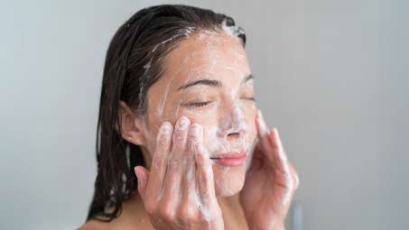 light skinned female presenting person washing face wtih scrub