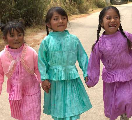 three medium skinned young girls in bright color dressed holding hands