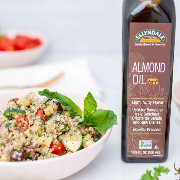 a white bowl with Greek quinoa salad, various colors and a bottle of NOW almond oil standing next to it