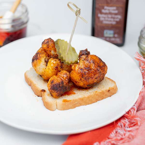 fryed cauliflower on a slice of bread centered on a white plate with a bottle of NOW Ellyndale Rice Bran Oil in the background and a pink napkin next to the plate