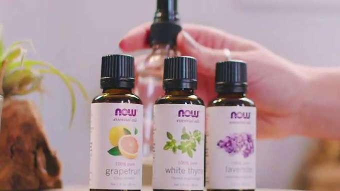 light skin hand grabbing an empty spray bottle with 3 bottles of NOW essential oils in front of it