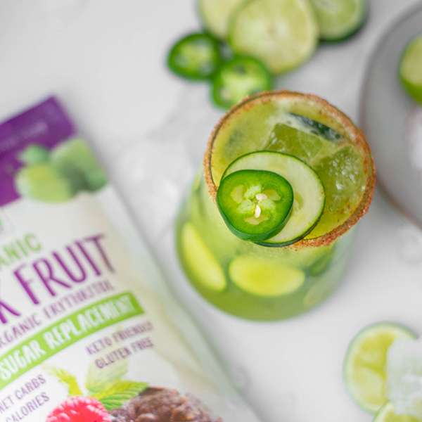 glass filled with a cucumber, jalapeno mocktail surrounded by limes and NOW Monk fruit package