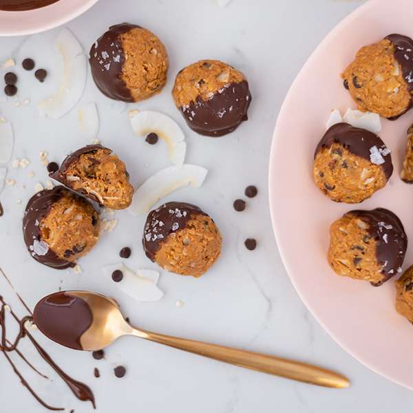 top view of Chocolate-Dipped Caramel Peanut Butter Oat Bites with spoon of chocolate and coconut oil