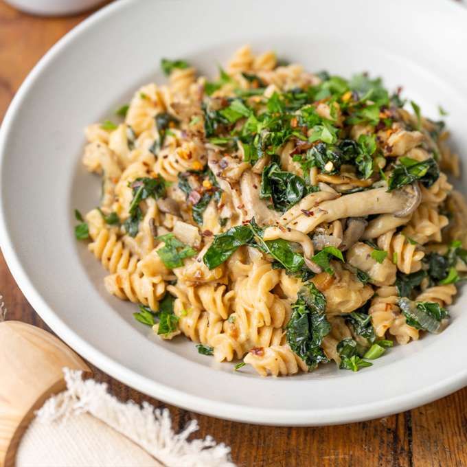 top view of a bowl of creamy wild mushroom kale rotini next to a boxs of NOW Rotini