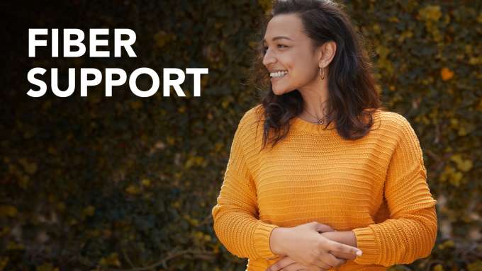 Side profile of a female smile, and overlapping on her stomach wearing a yellow sweater with bushes in the background.