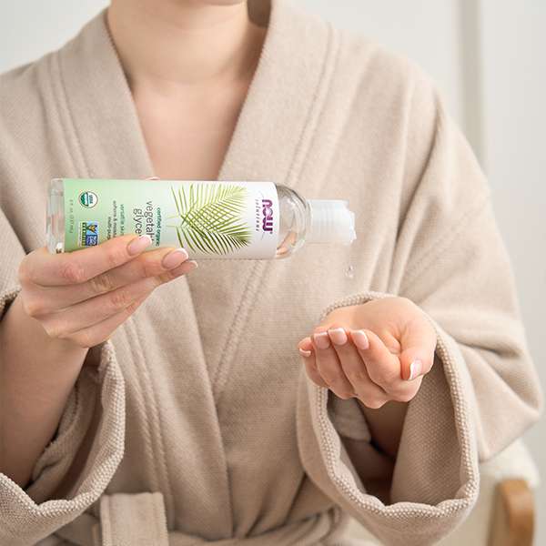 light skinned female presenting person pouring NOW Vegetable Glycerine into her hand wearing a brown robe