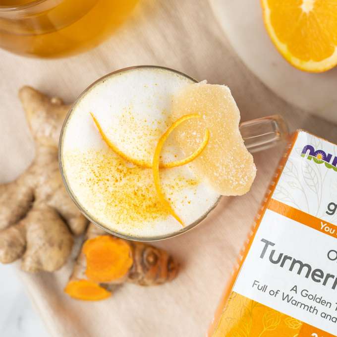 top view of creamy vanilla tumeric ginger tea latte with orange and ginger root next to it