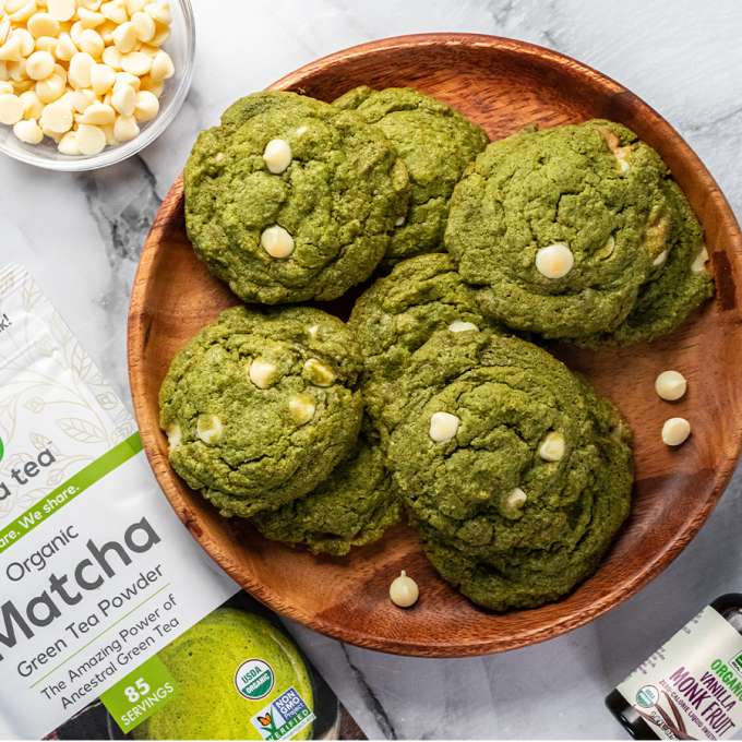 top view of matcha white chocolate cookies on wooden plate next to bag of NOW Matcha tea