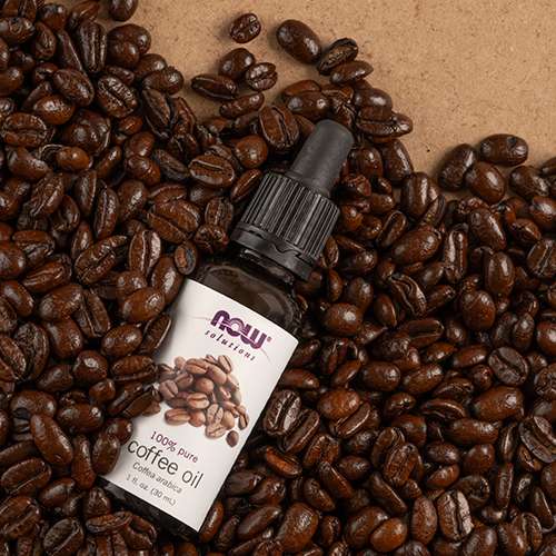 top view of NOW Coffee Oil with coffee beans to the left and tan background to the right