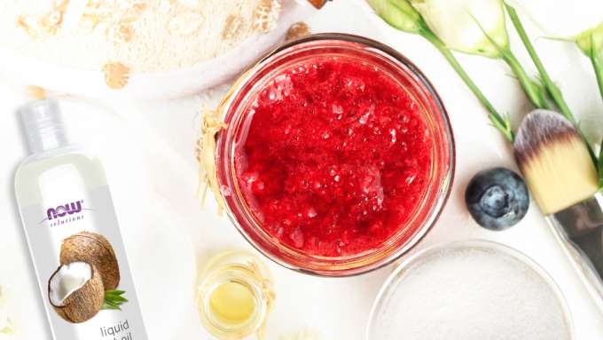 top view of red sugar scrub next to various beauty tools including NOW coconut oil