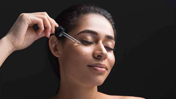 light-skinned, female-presenting person applying drops of skin serum to her face