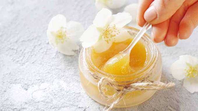jar with honey face mask with a light skinned hand holding a spoon