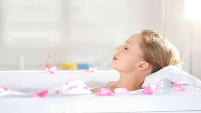 A female-presenting person with light skin and blonde hair relaxes in a bath.