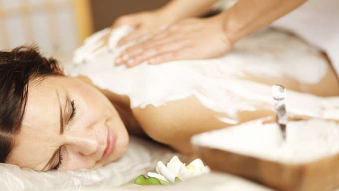 A female-presenting person lying face down, relaxed, receiving a massage with Cooling Body Scrub.