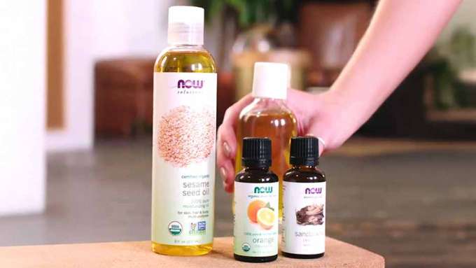 ingredients for detox massage oil including Sandalwood Oil blend, Orange Oil and an unamed carrier oil with a hand reaching in for a bottle of the mixed recipe