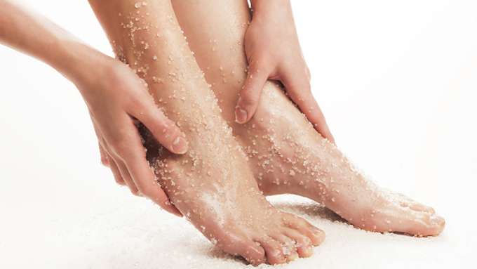 A person applying a foot scrub to their feet against a white background. 