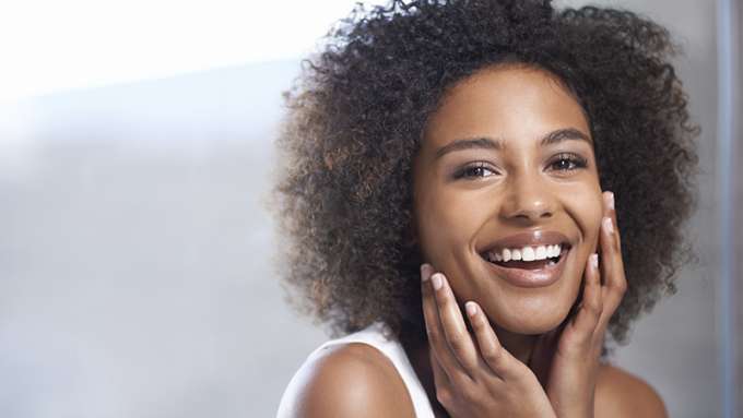 A female-presenting person with dark-skin, dark curly hair and brown eyes gently touching their face