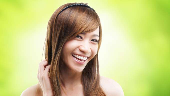 A female-presenting person with light skin and long brown hair is smiling at the camera