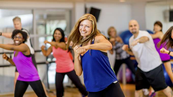 A female-presenting person with light skin, blonde hair and an athletic top leads a kickboxing class