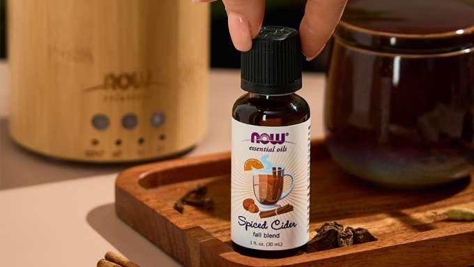close up shot of NOW Spiced Cider Essential Oil with fingers grabbing the top