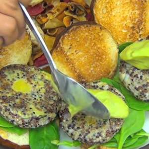 A hand offscreen scoops lime-green Avocado Puree onto a plate of Quinoa and Chia Sliders.