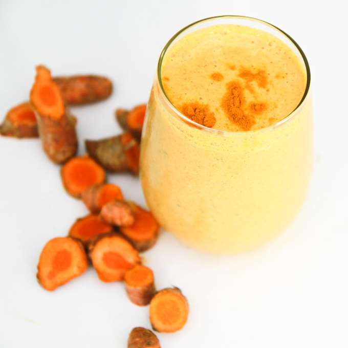 A tall, skinny drinking glass filled with a Creamy Vanilla Turmeric Smoothie.