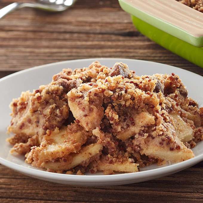 A white ceramic plate on a wooden table holds a serving of Gluten Free Apple Crisp.