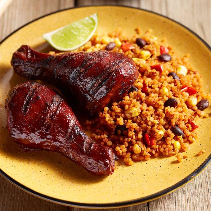 A yellow plate on a wooden table holds servings of Grilled BBQ Chicken with Quinoa.