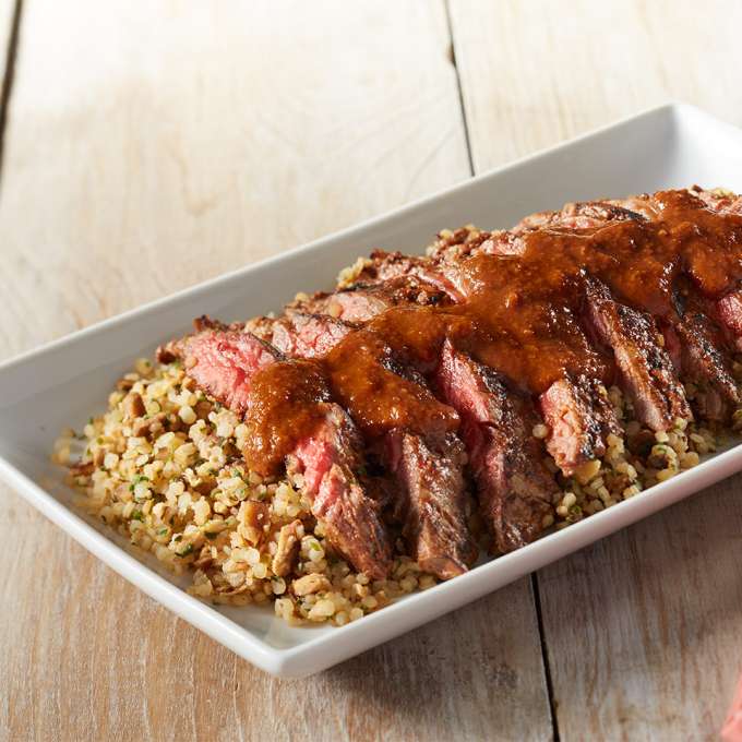 A white platter on a red placemat holds servings of Grilled Mole Steak Over Whole Grain Quinoa.